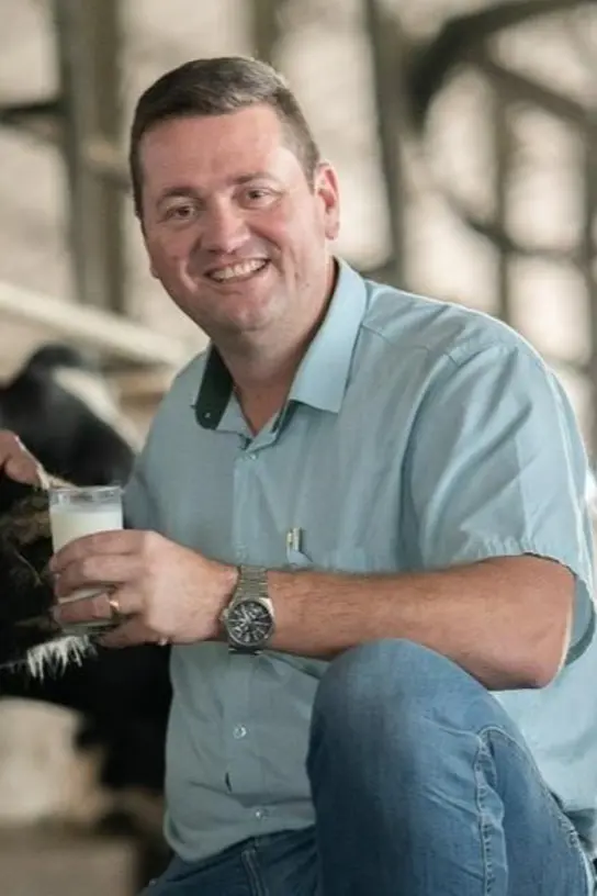 Produtor feliz ao lado da vaca e do leite fresco