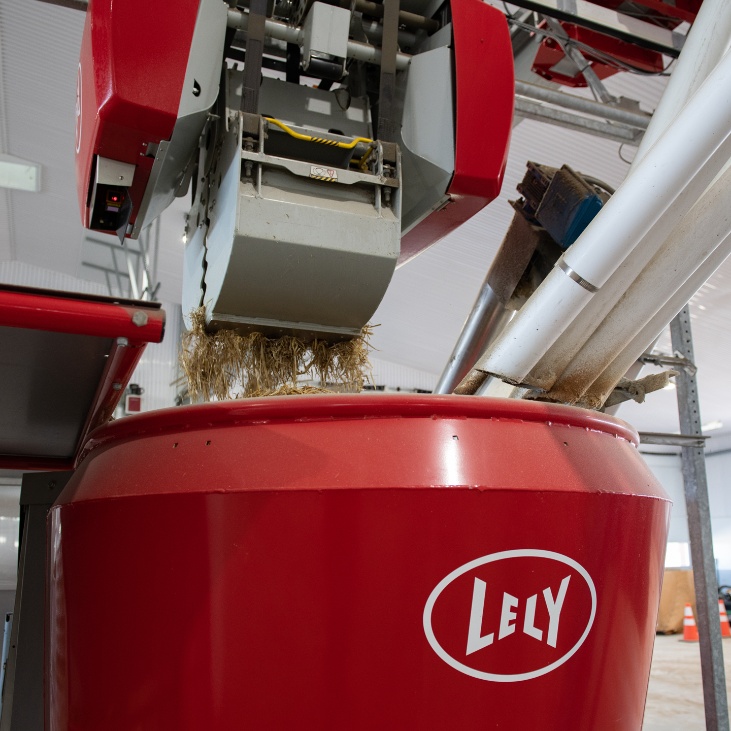 Un grappin à aliments Lely Vector dans une grange avec différents types d'aliments empilés les uns sur les autres.