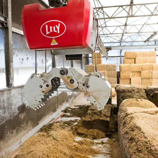 A Lely Vector feed grabber in a barn with different types of feed stacked on top of each other.